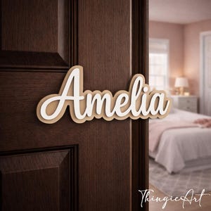 May include: A wooden sign with the name "Amelia" in a layered design. The top layer is white, and the bottom layer is a light brown. The sign is mounted on a dark brown door. The background shows a bedroom.