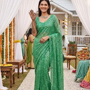May include: A vibrant emerald green saree fully covered in shimmering sequins. The garment features a classic drape with a pallu falling over the shoulder, a round neckline, and a fitted bodice, creating a cohesive and sparkling monochromatic look.