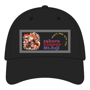 Peut inclure: Casquette de baseball noire avec un motif rectangulaire. Le motif représente un Shiba Inu en kimono, des fleurs de cerisier et le Mont Fuji. Le texte comprend "sakura kimono Mt. fuji" et "PRINTS MADE WITH LOVE."
