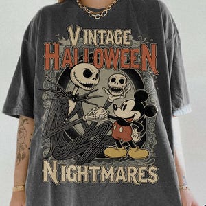 May include: A charcoal gray short-sleeve t-shirt featuring a graphic print with the text VINTAGE HALLOWEEN NIGHTMARES. The design depicts a tall skeletal figure holding a skull and a cartoon mouse character, set against an ornate circular frame.