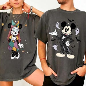 以下が含まれることがあります： ディズニーキャラクターが描かれた2枚のダークグレーのTシャツ。1枚はパッチワークデザインのミニーマウス、もう1枚はジャック・スケリントンに扮したミッキーマウスが描かれ、お化けとコウモリが周りに描かれています。どちらのシャツもヴィンテージ感があります。