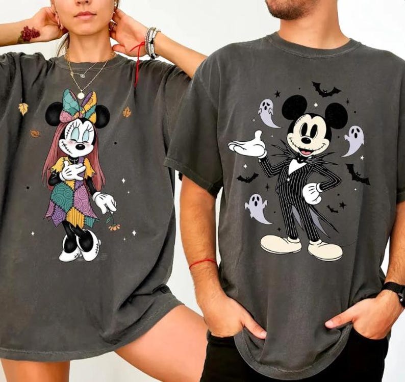 以下が含まれることがあります： ディズニーキャラクターが描かれた2枚のダークグレーのTシャツ。1枚はパッチワークデザインのミニーマウス、もう1枚はジャック・スケリントンに扮したミッキーマウスが描かれ、お化けとコウモリが周りに描かれています。どちらのシャツもヴィンテージ感があります。