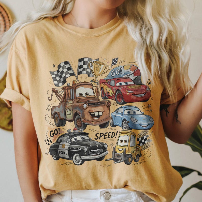 May include: A mustard yellow t-shirt featuring a graphic print of characters from the movie Cars, including a brown tow truck, a red race car with the number 95, a blue sports car, a black police car, and a yellow forklift, with the text GO and SPEED.