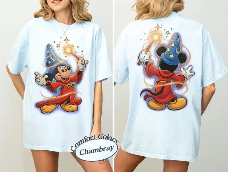 May include: Pale blue t-shirt with a front and back graphic of Mickey Mouse dressed as a sorcerer, holding a wand with stars. The shirt has short sleeves and a loose fit. The text "Comfort Colors Chambray" is on the bottom.