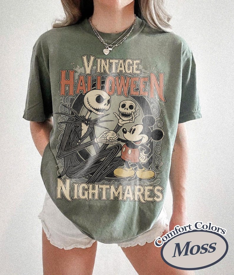 May include: A moss green short-sleeve t-shirt featuring a graphic print with the text VINTAGE HALLOWEEN NIGHTMARES. The design depicts a skeletal character holding a skull and standing next to a cartoon mouse character in a circular frame.