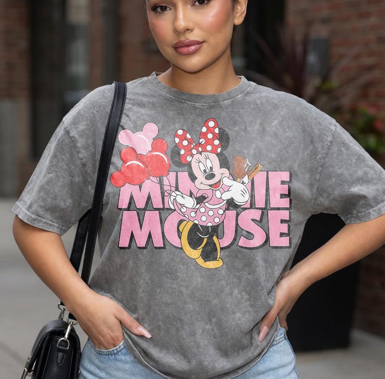 May include: Gray t-shirt featuring a Minnie Mouse graphic. The graphic includes Minnie Mouse holding balloons and a musical instrument, with the words "MINNIE MOUSE" in pink. The shirt has a vintage, washed look.
