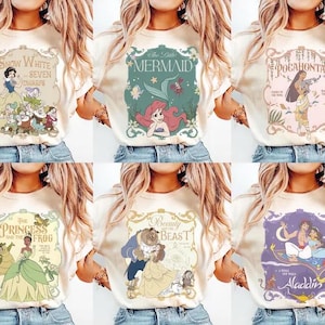 May include: Cream-colored t-shirts featuring various Disney princess designs. Each shirt showcases a different princess, including Snow White, Ariel, Pocahontas, Tiana, Belle, and Jasmine, with their respective movie titles. The designs are in a vintage, storybook style.