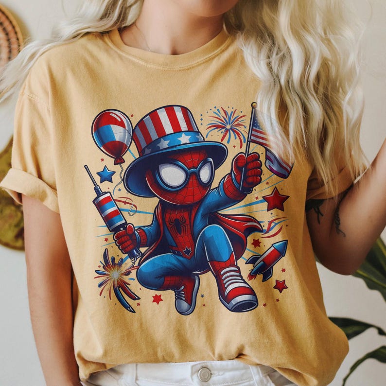 K&ouml;nnte beinhalten: Senfgelbes T-Shirt mit einer Cartoon-Figur von Spider-Man in einem patriotischen Outfit. Die Figur tr&auml;gt einen Zylinder und einen Umhang und h&auml;lt eine Flagge und ein Feuerwerk. Das Design verwendet rote, wei&szlig;e und blaue Akzente mit Feuerwerk und Sternen.