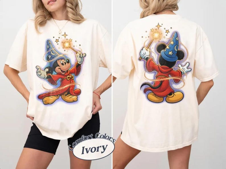 May include: Ivory t-shirt with front and back graphics of Mickey Mouse as a sorcerer. Mickey is in a blue wizard hat and red robe, holding a wand. The shirt is a Comfort Colors brand.