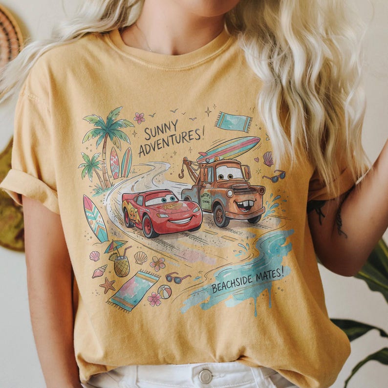 May include: A mustard yellow t-shirt featuring a graphic print of Lightning McQueen and Mater from Cars driving on a beach road. The design includes palm trees, surfboards, a pineapple drink, and the text Sunny Adventures and Beachside Mates.