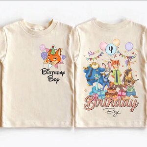 K&ouml;nnte beinhalten: Zwei cremefarbene T-Shirts mit kurzen &Auml;rmeln. Ein Shirt zeigt einen Cartoon-Fuchs mit Partyhut und dem Text "Birthday Boy". Das andere Shirt hat eine Gruppe von Cartoon-Charakteren, Luftballons und den Text "Birthday Boy".