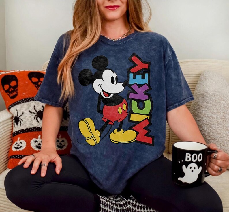 May include: A navy blue t-shirt featuring Mickey Mouse with the word "MICKEY" in colorful letters. The shirt is paired with black leggings. A black mug with a white ghost and the word "BOO" is also visible.