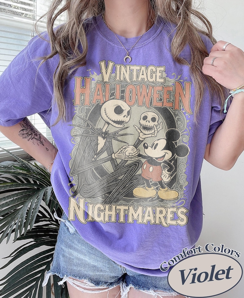 May include: A violet t-shirt featuring a graphic print with the text VINTAGE HALLOWEEN NIGHTMARES. The design depicts a tall skeletal figure in a pinstripe suit holding a skull, standing next to a cartoon mouse character in red shorts and yellow shoes.