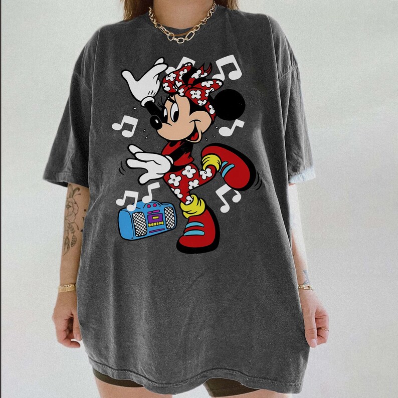 Pu&ograve; includere: T-shirt grigio scuro con grafica di Minnie Mouse che balla. Minnie indossa un completo rosso con dettagli floreali bianchi, scarpe rosse e un fiocco rosso. &Egrave; presente anche un boombox blu e note musicali.