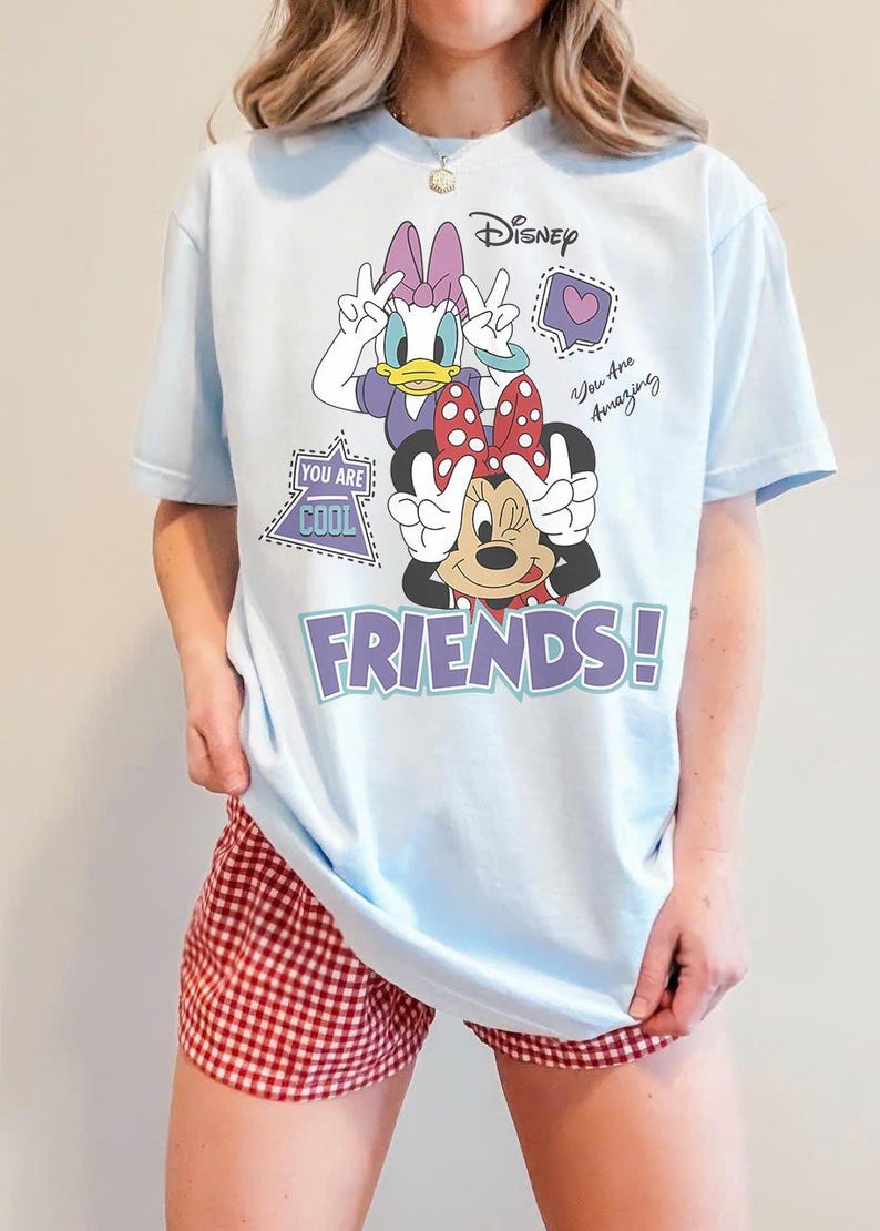 Może przedstawiać: Jasnoniebieska koszulka z Daisy Duck i Minnie Mouse z Disneya ze słowem "FRIENDS!" w kolorze fioletowym. Koszulka ma dodatkowy tekst z napisem "You Are Cool" i "You Are Amazing".