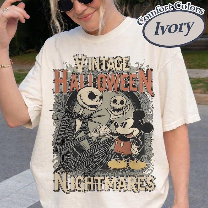 May include: An ivory t-shirt featuring a graphic print with the text Vintage Halloween Nightmares. The design depicts a tall skeletal figure in a pinstripe suit holding a skull, standing next to a cartoon mouse character in red shorts and yellow shoes.