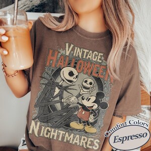 May include: A brown t-shirt featuring a graphic print with the text VINTAGE HALLOWEEN NIGHTMARES. The design depicts a skeletal figure in a pinstripe suit holding a small skull, standing next to a cartoon mouse character in red shorts and yellow shoes.