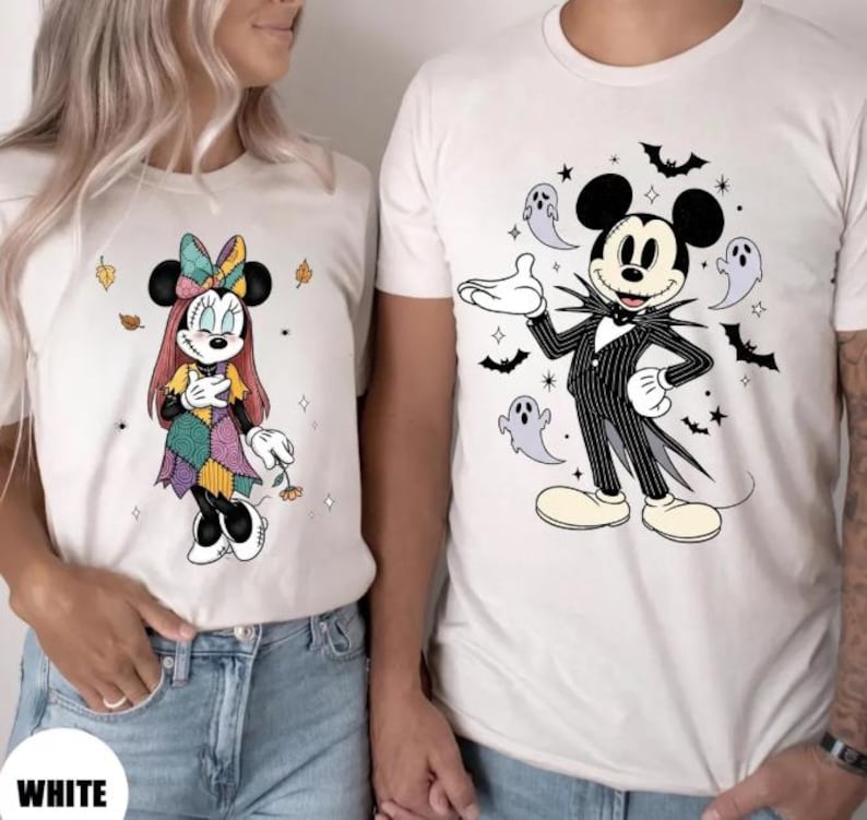 以下が含まれることがあります： ディズニーキャラクターが描かれた白いTシャツ。1枚はパッチワークのドレスを着たミニーマウス、もう1枚はコウモリと幽霊に囲まれたジャック・スケリントンに扮したミッキーマウス。下部には「WHITE」の文字。