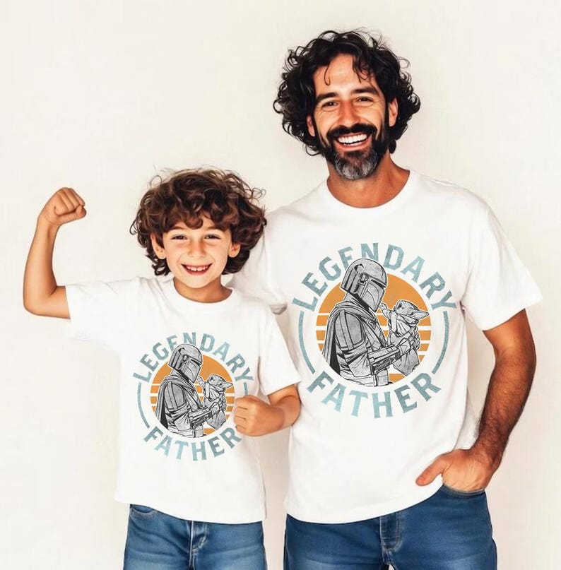 K&ouml;nnte beinhalten: Zwei wei&szlig;e T-Shirts mit dem Text "LEGENDARY FATHER" und einer Grafik eines Charakters, der ein Baby h&auml;lt. Die Shirts werden von einem Mann und einem Kind getragen. Die Grafik befindet sich in einem Kreis mit orangefarbenem Hintergrund.