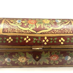 May include: A rectangular wooden chest with a domed lid, featuring a deep red base color with hand-painted floral motifs in yellow, green, orange, and blue. The edges are accented with gold paint, and a central metal latch secures the front closure.