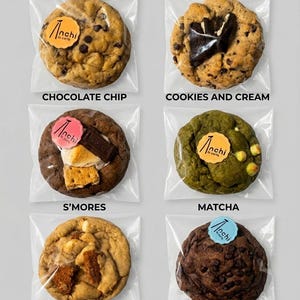 May include: Six individually packaged cookies. Flavors include chocolate chip, cookies and cream, S'mores, matcha, Biscoff, and double chocolate. Each cookie is round and has a unique topping or ingredient. Each package has a circular sticker with the brand name.