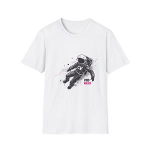 May include: White t-shirt featuring a black and gray illustration of an astronaut floating in space. The astronaut is wearing a spacesuit and helmet. The text "VOID WALKER" is printed in pink.
