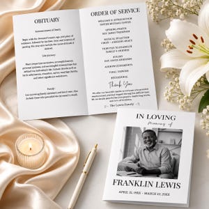 May include: A funeral programme template featuring an open booklet with an order of service and a closed booklet displaying a black and white portrait of a man named Franklin Lewis, accompanied by a white pen and a lit candle in a glass holder.