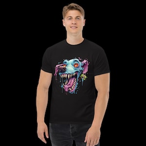 Könnte beinhalten: Schwarzes T-Shirt mit einem farbenfrohen Cartoon-Hundekopf-Design. Der Hund hat blaues Fell, rosa Ohren und eine lange, rosa Zunge. Seine Augen sind orange und er hat scharfe weiße Zähne. Die Grafik hat einen tropfenden Farbeffekt.