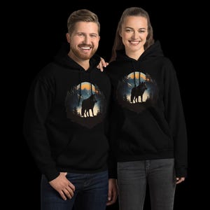 May include: Black hooded sweatshirts featuring a wolf design. The graphic shows a wolf silhouette against a backdrop of mountains, trees, and a sunset. The sweatshirts have a front pocket and a drawstring hood.