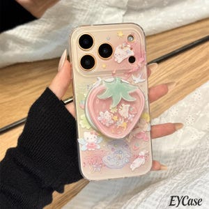 Puede incluir: Funda transparente para teléfono con diseño de fresa rosa y personajes de dibujos animados. La funda tiene un agarre desplegable y una parte trasera transparente.