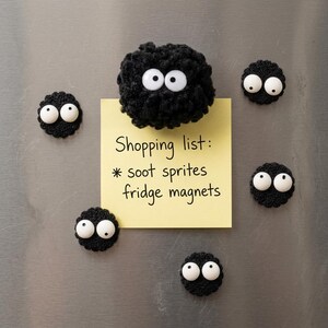 May include: Six black crocheted soot sprite fridge magnets with white plastic googly eyes. One larger fuzzy magnet holds a yellow square sticky note with the handwritten text: Shopping list: * soot sprites fridge magnets.