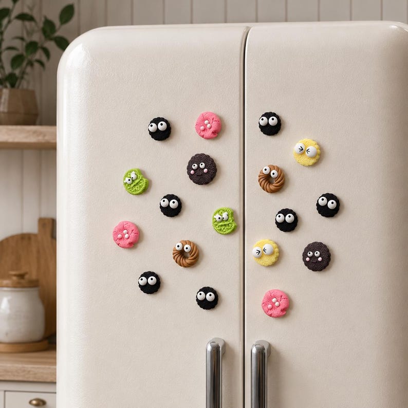 May include: A collection of small, round refrigerator magnets shaped like cookies and circular treats in various colors including black, pink, green, yellow, and brown. Each piece features two white plastic googly eyes attached to the surface.