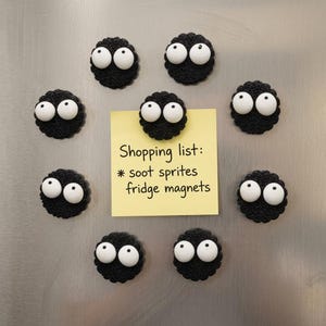 May include: Eight round, black, crocheted fridge magnets with large, white, googly eyes. One magnet holds a yellow square sticky note with the handwritten text: Shopping list: * soot sprites fridge magnets. The magnets are arranged in a circle.