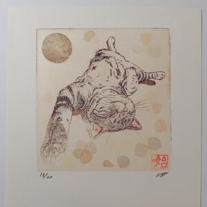 May include: An art print depicting a cat on its back, with a light brown circle and abstract shapes in the background. The cat is in shades of brown and grey, with its eyes closed. The print is numbered 15/20 and signed.