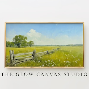 May include: A framed landscape painting shows a field with a wooden fence, trees, and a blue sky with clouds. The artwork is in a gold frame. The text "THE GLOW CANVAS STUDIO" is below the frame.