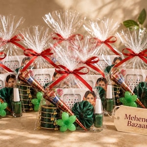 Könnte beinhalten: Eine Sammlung von Geschenksets, verpackt in durchsichtiger Cellophanfolie mit roten Schleifen. Jedes Set enthält eine Henna-Tüte, dunkelgrüne Armreifen, grünen Nagellack, ein grünes Stoff-Haargummi und eine Packung mit Bindi-Aufklebern.