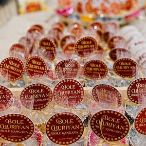 May include: Multiple sets of bangles individually wrapped in clear plastic, each topped with a circular maroon tag featuring gold text that reads BOLE CHURIYAN BOLE KANGANA. The bangles come in various colors including red, white, pink, and green.