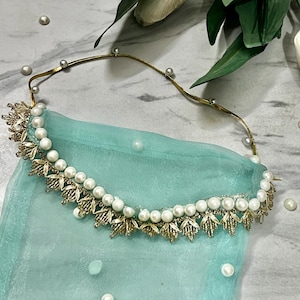 Può includere: Un cerchietto color oro con una fila di perle artificiali bianche e dettagli metallici dorati a forma di foglia. Il cerchietto è fissato a un velo in tessuto trasparente verde menta chiaro, decorato con perle artificiali bianche sparse.