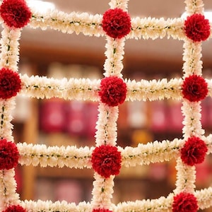 May include: A decorative floral grid hanging made of white jasmine flower garlands arranged in a square lattice pattern, accented with vibrant red carnation blossoms at each intersection and along the top horizontal border.