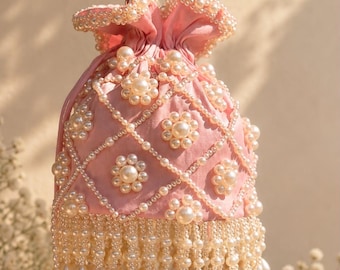 May include: A light pink drawstring pouch bag featuring a lattice pattern of white faux pearls. The bag is adorned with floral-shaped pearl clusters and a dense fringe of dangling teardrop and round pearls at the base, with a pearl handle.