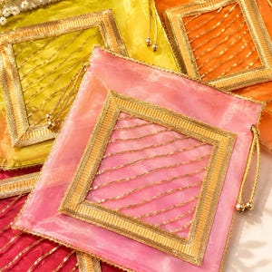 Peut inclure: Une collection de pochettes carrées à cordon de serrage en tissu translucide rose, jaune, orange et rouge. Chaque pochette présente un cadre carré central avec une bordure métallique dorée et des fils dorés en diagonale, avec des perles dorées.