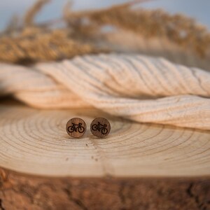 Könnte beinhalten: Ein Paar runde Ohrstecker aus Holz mit einer dunkelbraunen, lasergravierten Fahrradgrafik auf der Vorderseite. Die Ohrringe haben eine natürliche Holzmaserung und eine flache, runde Form, die eine detaillierte Fahrradsilhouette zeigt.