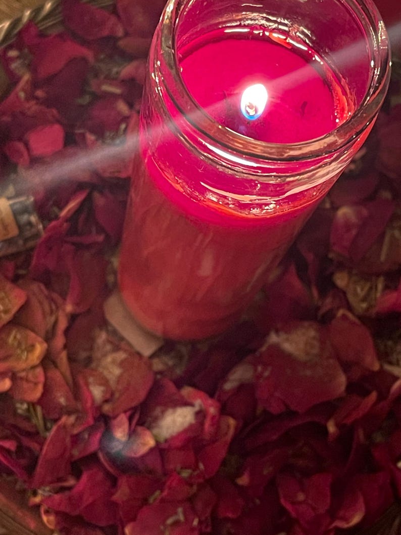 Puede incluir: Una vela roja encendida en un tarro de cristal transparente, rodeada de p&eacute;talos de rosa rojos secos. La llama de la vela brilla intensamente, creando una luz c&aacute;lida. La escena evoca un ambiente m&iacute;stico.