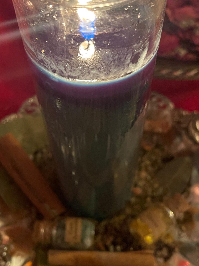 Puede incluir: Una vela azul oscuro encendida en un vaso transparente. La vela se encuentra sobre una bandeja decorativa plateada con palitos de canela, piedras peque&ntilde;as y una botella peque&ntilde;a. La llama de la vela es brillante y la cera tiene una apariencia texturizada.