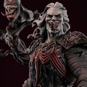 May include: A detailed statue of a character with pale skin, red eyes, and long white hair. The figure has a menacing grin, a long tongue, and a symbiote-like design on the chest. A smaller, monstrous figure is attached to the main character.