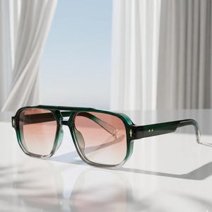 May include: Aviator-style sunglasses in green and clear with gradient lenses. The sunglasses feature a double bridge and a thick frame. The lenses transition from light orange to clear. The sunglasses are set against a bright background.