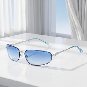 May include: Rimless sunglasses with a gradient blue tint. The frames are silver with light blue temples. The lenses are a rectangular shape. The sunglasses are sitting on a white surface.