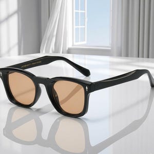May include: Black sunglasses with square frames and light brown lenses. The sunglasses have a classic design with a modern twist. The text "JACKIE WITT FORME DESIGN" is printed on the top of the frame.
