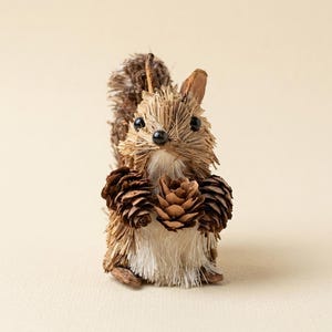 May include: A handcrafted squirrel figurine made of natural materials. The squirrel has a brown body, a fluffy tail, and is holding two pine cones. The eyes are black beads. The figurine is a decorative item.