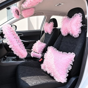 以下が含まれることがあります： ピンク色の車のアクセサリーセット。ステアリングホイールカバー、ヘッドレストカバー、シートベルトカバー、小さなクッションが含まれています。柔らかいフリル素材で作られており、車の内装に装飾的なアクセントを加えています。